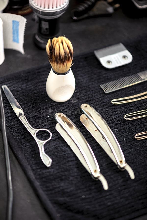 Traditional barbershop tools including straight razors, shaving brush, and scissors arranged on black towel